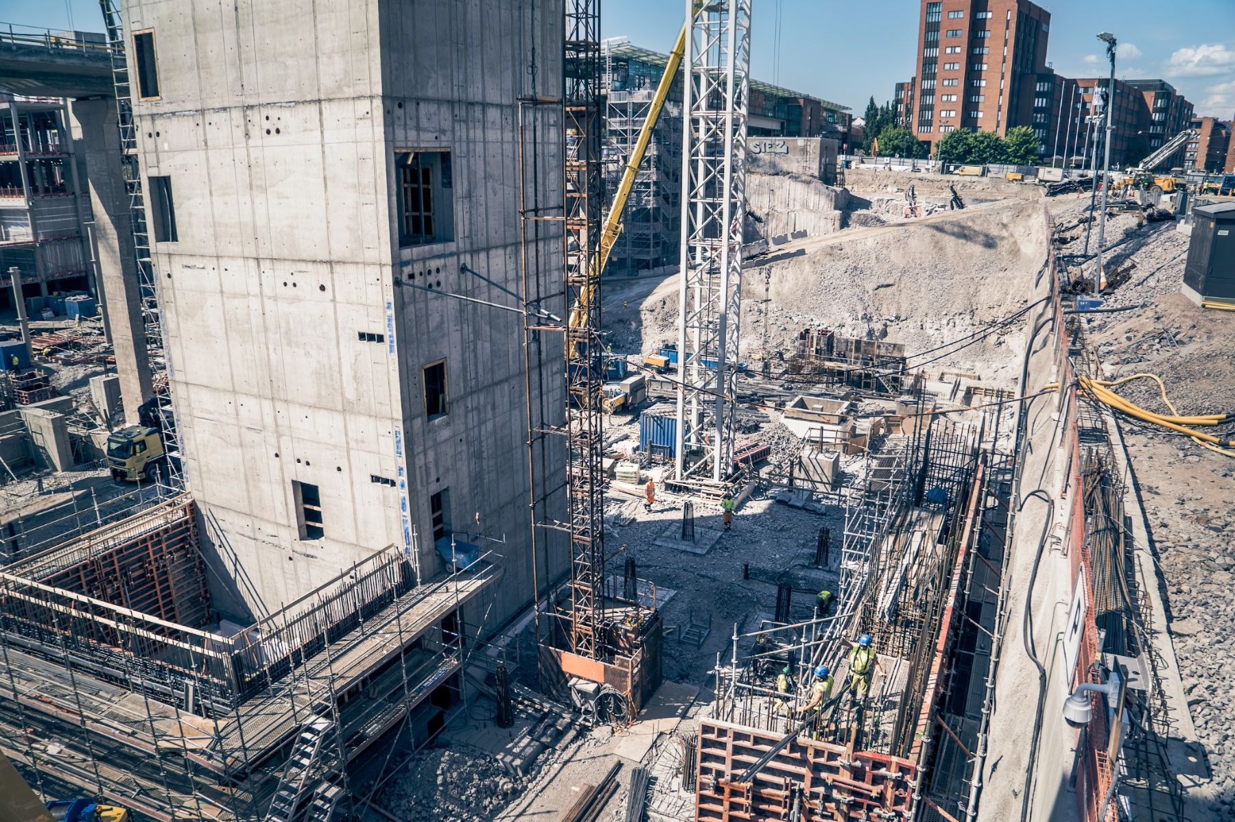 Ilmakuva betonisesta runkorakenteesta rakennustyömaalla, jossa nosturi laskee materiaalia kaivantoon
